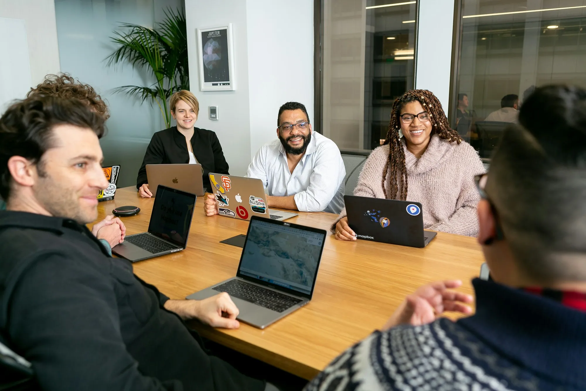 Business owners with laptops talking around a wooden table in a bright meeting room