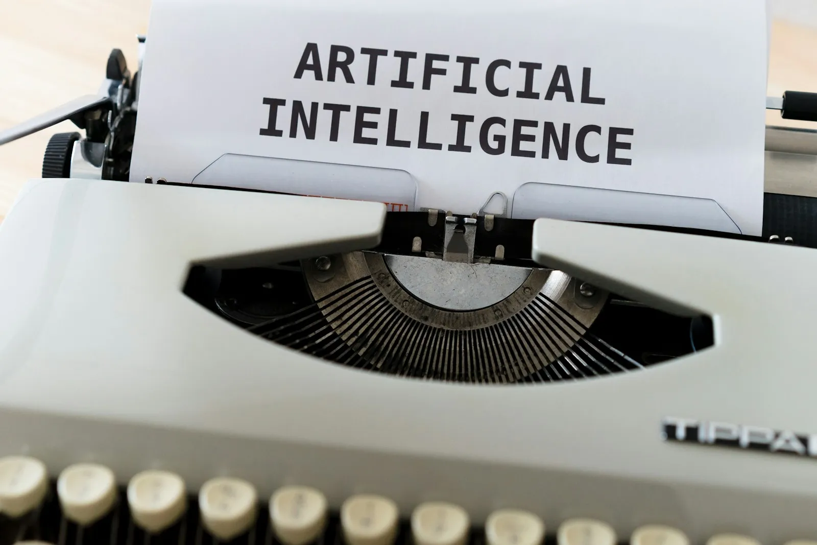 A vintage off-white typewriter holding a sheet of paper printed with the words ARTIFICIAL INTELLIGENCE in bold black letters