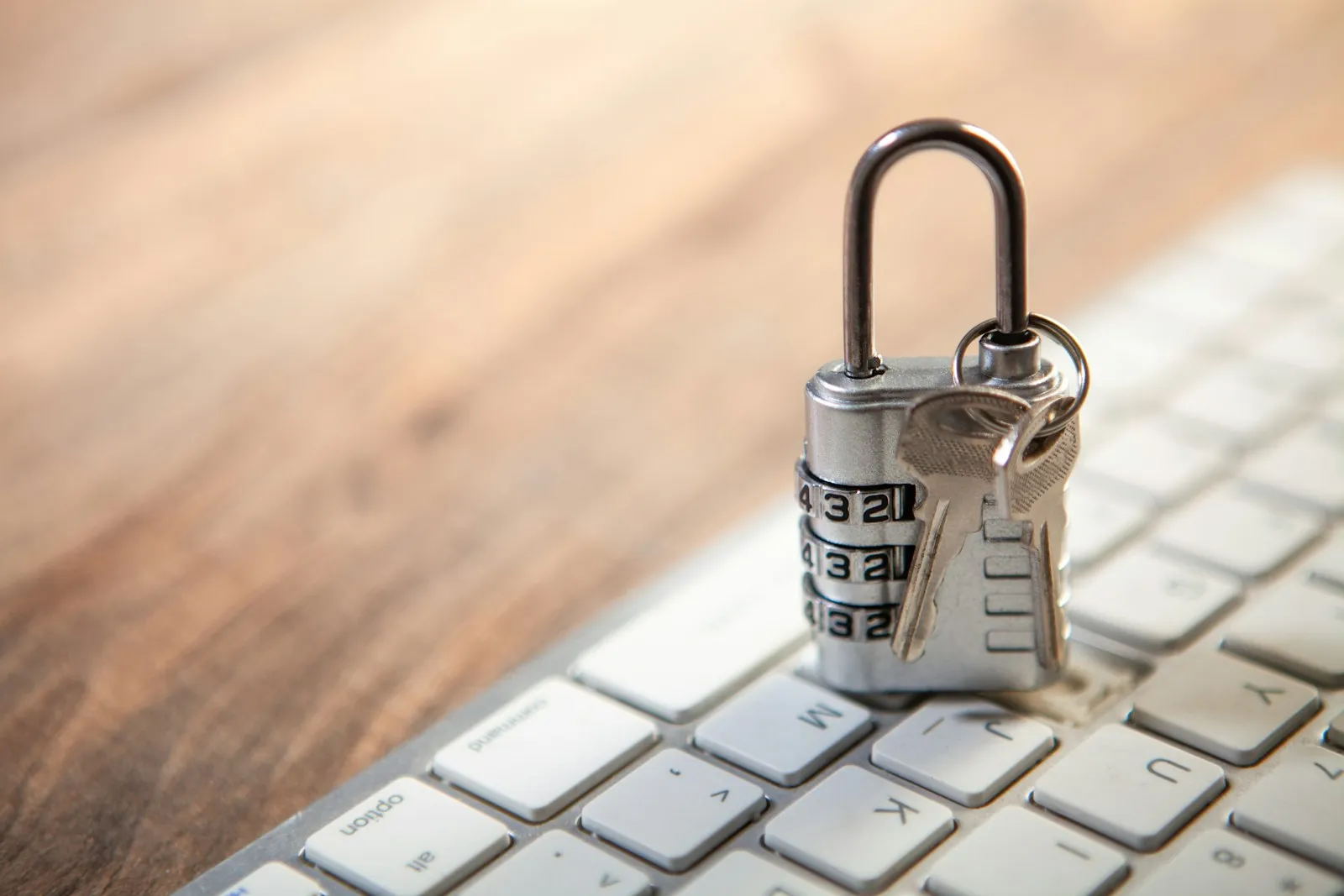 A silver combination padlock with keys resting on a white computer keyboard