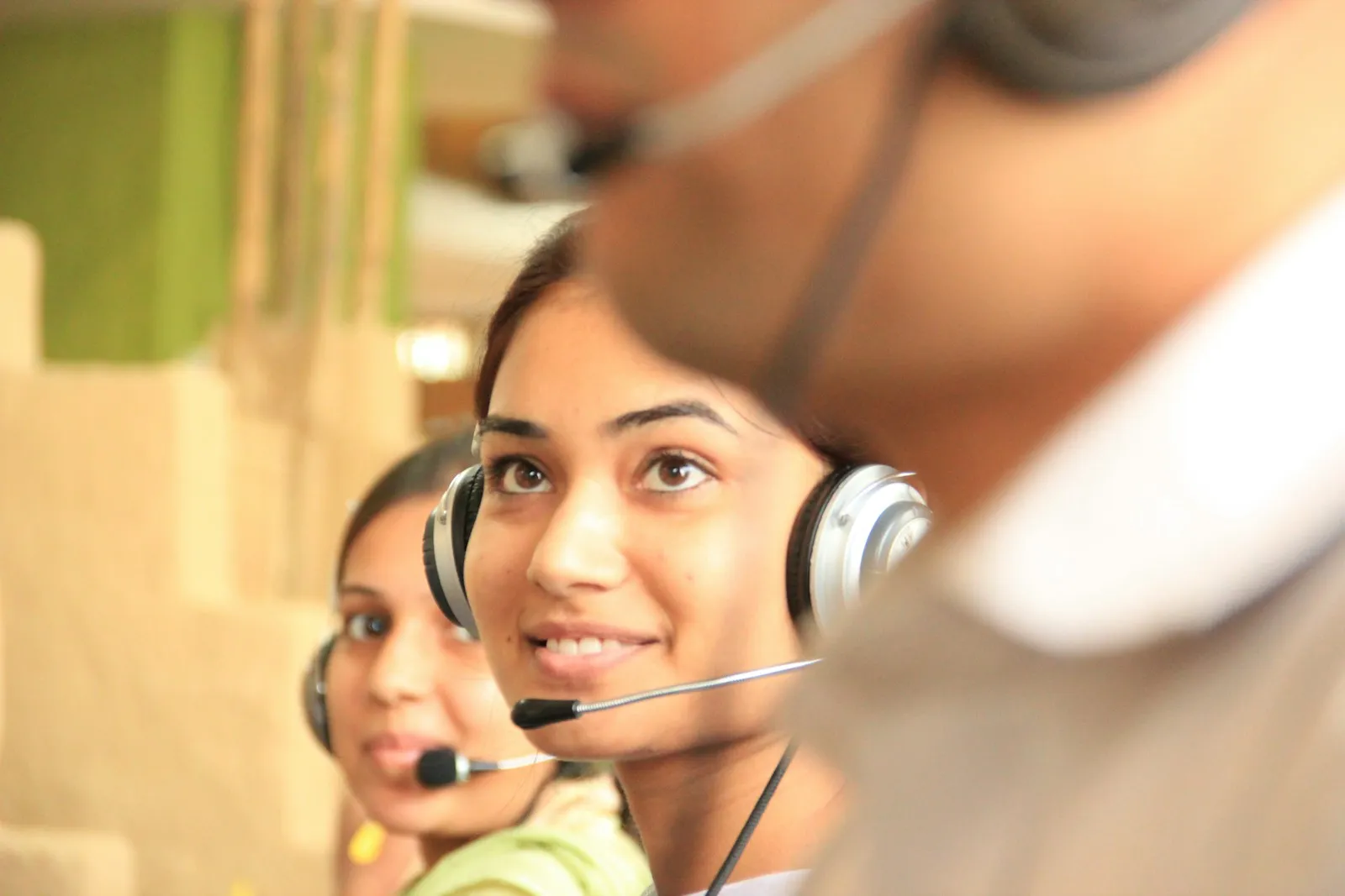 Two smiling women wearing headsets working together in a bright office